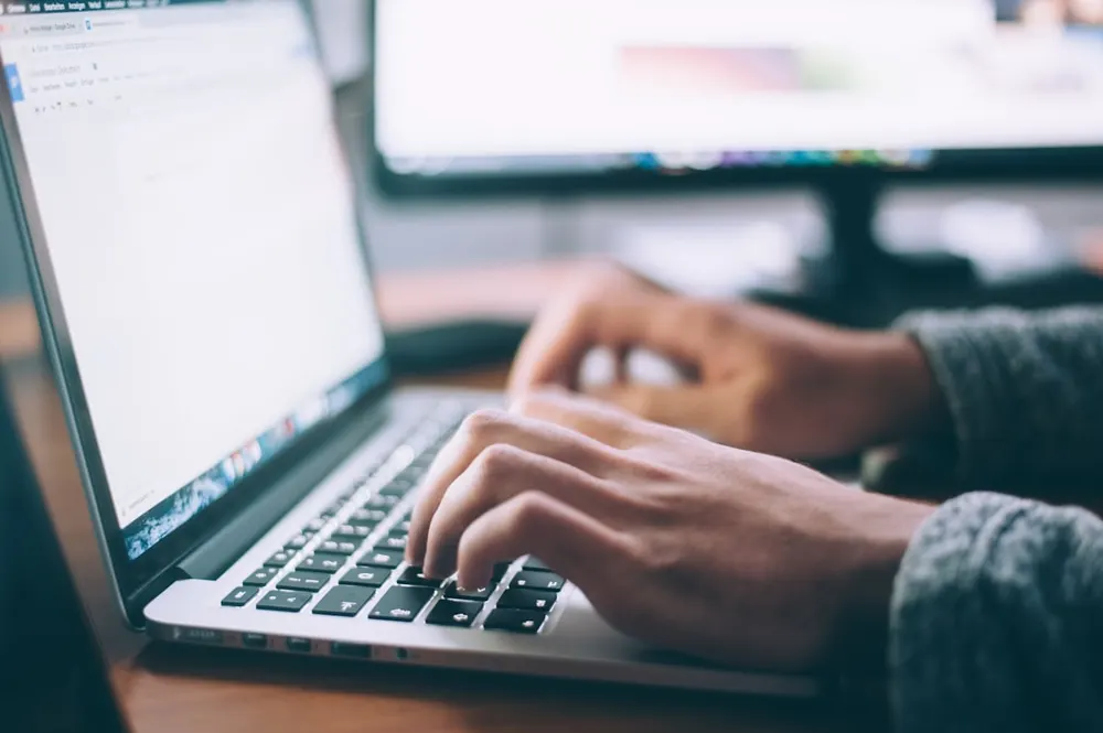 Hands resting on a laptop keyboard in front of a blank document, unable to start working