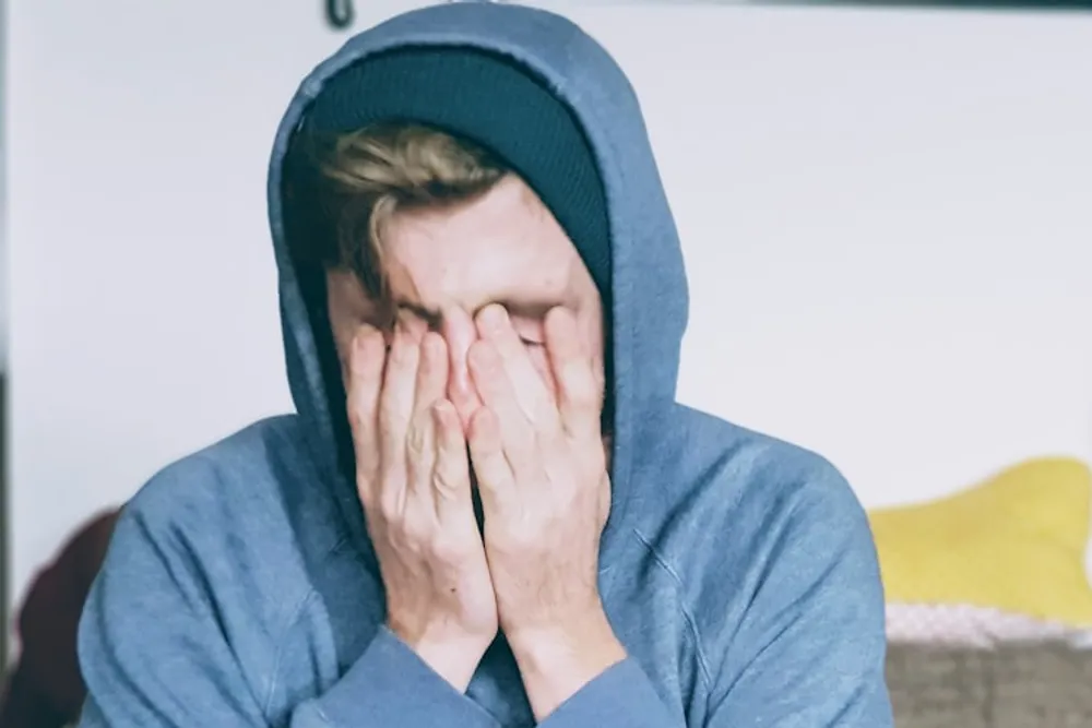 Tired person sitting with both hands over their face, struggling to think clearly through brain fog