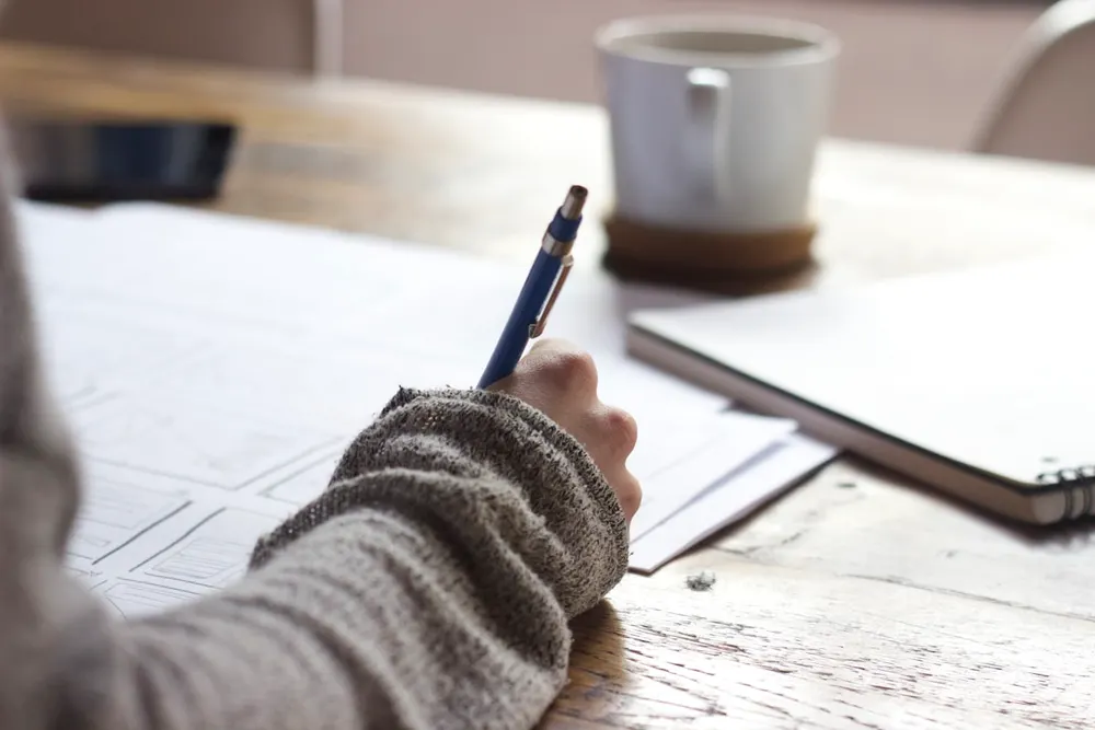 Student writing notes by hand at a desk with a cup of coffee during a study session